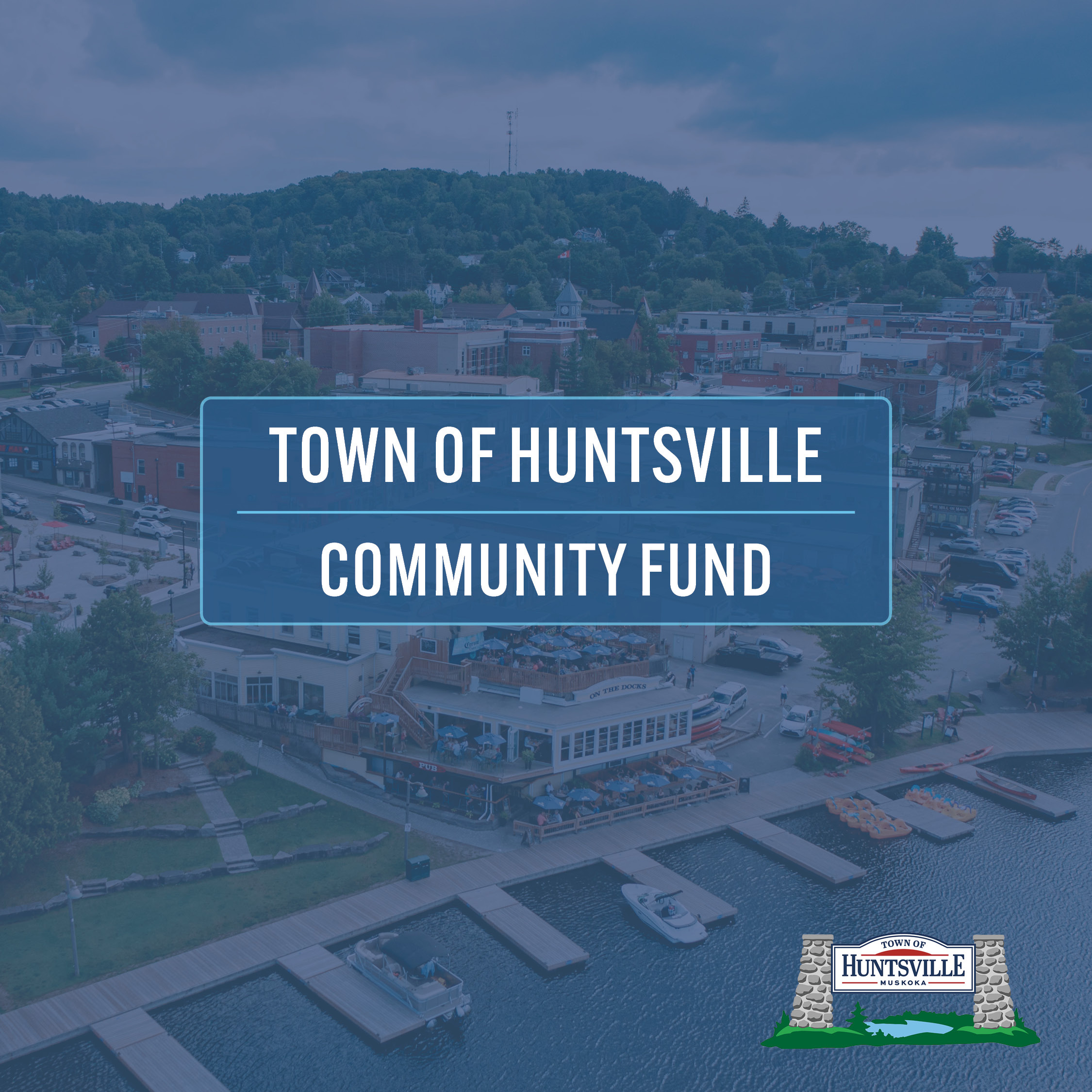 Aerial view of downtown Huntsville’s waterfront with a blue overlay. Center text reads “Town of Huntsville Community Fund,” with the Town of Huntsville logo in the bottom right corner.
